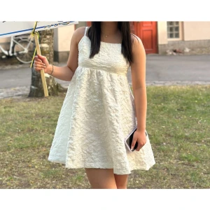 Vit kort klänning med struktur - Säljer en söt vit kortklänning med axelband och fyrkantig ringning. Klänningen har en strukturerad yta och är lätt utsvängd för en luftig känsla. Perfekt för varma dagar och studentfirande!