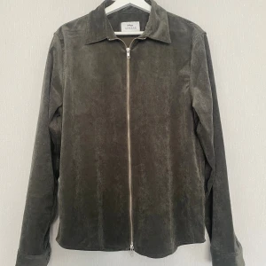 Olivgrön manchester overshirt från Ciszere - Snygg olivgrön overshirt från Ciszere i mjuk manchester. Rak passform med klassisk krage och hel dragkedja framtill. Långärmad modell som passar perfekt över en t-shirt. Stilren och enkel att matcha till olika outfits.