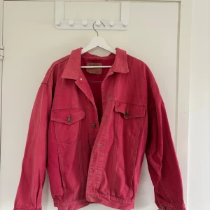 Rosa vintage jeansjacka från Anvil, stl L - Min mormors gamla jacka. Snygg rosa jeansjacka från Anvil med klassisk krage, två bröstfickor med knappar och justerbara knappar i midjan. Jackan har en loose passform och är tillverkad i bomull. Perfekt för dig som vill sticka ut med färg i din outfit.