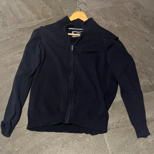 zip tröja från Bugatti  - Säljer en stilren mörkblå kofta från Bugatti i mjukaste bomull. Koftan har dragkedja framtill, ribbade muddar och hög krage. Perfekt att slänga på sig när det är lite kyligt ute. Enkel och klassisk design som funkar till det mesta.