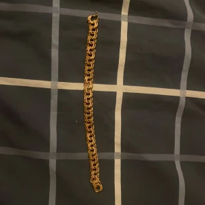 Chunky guldarmband med kedjelänkar - Säljer ett chunky armband i guldton med grova, rundade kedjelänkar som ger en cool och lyxig vibe. Perfekt för dig som gillar statement-smycken och vill sticka ut. Länkarna är tätt sammanlänkade och har en snygg glansig finish.