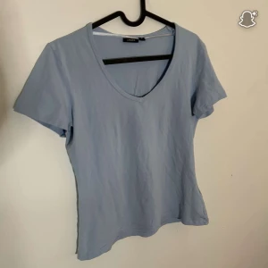 Ljusblå t-shirt med v-ringning Lindex - En basic ljusblå t-shirt från Lindex i storlek M. T-shirten har v-ringad hals och korta ärmar, perfekt för en chill och enkel stil. Tillverkad i mjuk bomull som känns skön mot huden.