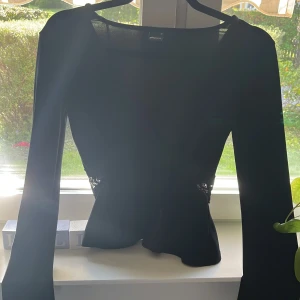 Oanvänd Svart omlottopp med spets Gina Tricot XS  - Supersnygg svart omlottopp från Gina Tricot i storlek XS. Toppen har långa ärmar och en markerad midja med bred spetsdetalj över magen. Mjuk och stretchig känsla, perfekt till jeans eller kjol. V-ringad framtill för en extra stylish look.
