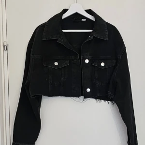 Svart croppad jeansjacka - Svart croppad jeansjacka från H&M med rå fransad nederkant & Silverfärgade knappar med bröstfickor. Jackan har en loose oversized fit.                                                       Använd få gånger. Väldigt fint skick. Strl L