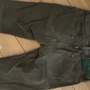 Grå/gröna jeans från Jacob Cohen, stl 32 - Säljer ett par grå jeans från Jacob Cohen i storlek 32. Byxorna har klassisk femficksdesign, raka ben och snygga detaljer vid fickorna. Tillverkade i bomull med en skön passform och diskret logga på myntfickan. Perfekta för en stilren och avslappnad look.