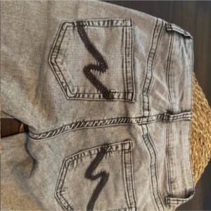 Grå lågmidjade jeans  - Snygga grå jeans från Nelly med lågmidja  och cool svart zigzag-detalj på bakfickorna. Liten skada som syns på bild annars i nyskick, använda en gång! Flyttar så vill ha så snabb affär som möjligt 