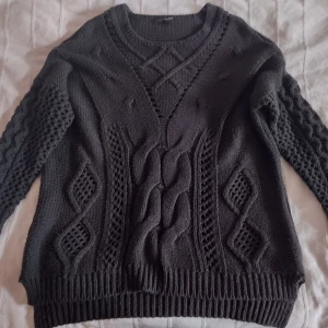 Mörkgrön stickad tröja med flätmönster - Mörkgrön stickad tröja från KappAhl med snygga flätmönster och strukturstickade detaljer framtill. Tröjan har långärmade ärmar med coolt hålmönster och ribbade muddar. Den är lite längre i modellen och längre i bak än i fram - perfekt för dig som gillar en mysig och stilren look. Den är ganska nopprig/luden. Storlek 40/42.