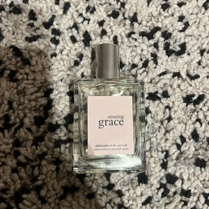 Philosophy Amazing Grace parfym 60 ml - Fräsch och feminin parfym från Philosophy, Amazing Grace. Ungefär 80% kvar i flaskan. Flaskan är fyrkantig i genomskinligt glas med en silvrig metallkork och ljus etikett framtill. Innehåller 60 ml. Doften är lätt och klassisk, perfekt för dig som gillar subtil elegans.