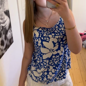 Blåvit blommig linnetopp med knytband - Snygg blå och vit linnetopp med stora blommor och smala axelband som knyts på axlarna. Toppen har en lös passform och är perfekt för varma dagar. Mönstret är riktigt somrigt och materialet känns lätt och luftigt.