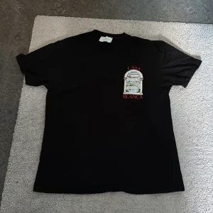 Svart t-shirt från Casablanca. Går att tvätta i maskin använd gärna en tvättpåse går att förhandla  - Svart t-shirt från Casablanca med färgglatt tryck av en arkad och landskap på ryggen samt mindre tryck framtill. T-shirten har rund hals och korta ärmar. Materialet är mjukt och känns som bomull. Perfekt för dig som gillar unika prints och streetstyle.