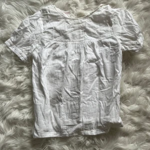 Vit blus från Esprit i bomull - Säljer en söt vit blus från Esprit i tunn bomull med diskreta ränder i tyget. Blusen har korta puffärmar och rund halsringning, samt fina sömdetaljer över bröstet. Perfekt för en fräsch och enkel look!