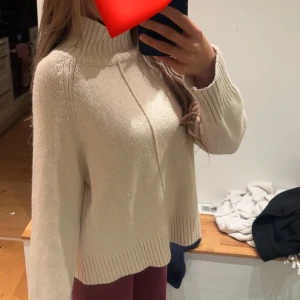 Beige stickad polotröja - Supermysig beige stickad polotröja med bred ribbad krage och muddar. Tröjan har en relaxed fit och långa ärmar, perfekt för kyliga dagar. Enkel att styla och passar till allt. Snygg detaljsöm framtill.
