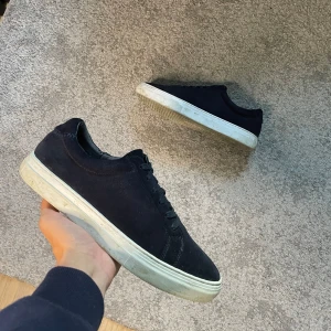 Vagabond skor  - Stilrena sneakers från Vagabond i mocka med vita, platta sulor. Skorna har rund tå och klassisk snörning. Perfekta för dig som gillar en clean och enkel look med en touch av premiumkänsla.