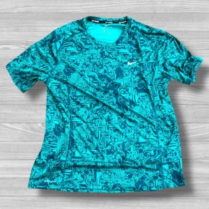 Nike Dri-Fit  - Snygg turkos t-shirt från Nike med digitalt mönster och Dri-Fit material som andas. Perfekt för träning och sport, med korta ärmar och rund hals. Nike-loggan i vitt på bröstet ger en sportig vibe. Skön passform och lätt känsla.