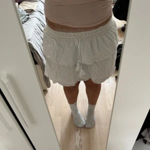 Vit volangkjol  - Supersöt vit kortkjol från Gina Tricot med volanger och snörning i midjan. Kjolen har små guldiga prickar som ger lite extra glans och är gjord i mjuk bomull. 