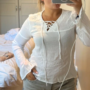 Vit blus med snörning  - Supersöt vit blus från Angelology lager 157 i tunn, lätt krinklad bomull. Långärmad modell med v-ringning och snygg snörning framtill. Perfekt för dig som gillar en chill och luftig stil. Ärmarna har lite utsvängd känsla för extra vibe.