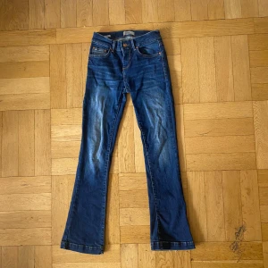 Blå bootcut jeans från LTB - Snygga blå jeans från LTB med klassisk bootcut passform och kontrastsömmar. Jeansen har fem fickor, normal midja och coola detaljer på bakfickorna. Perfekt för dig som gillar en tidlös och avslappnad stil. Materialet är mjukt jeans och färgen är mörkblå med lätt slitning. Storleken är w25 L30.