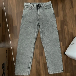 Weekday Galaxy Loose Straight Jeans grå - Grå stentvättade jeans från Weekday i modellen Galaxy Loose Straight. Jeansen har en rak och loose passform med klassiska fem fickor och tillverkade i ekologisk och återvunnen bomull. Perfekta för en avslappnad och trendig look. JEANSEN HAR ALDRIG ANVÄNTS!