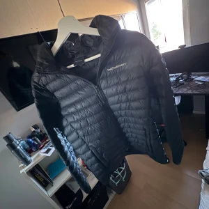 Svart dunjacka Peak Performance  - Säljer en svart dunjacka från Peak Performance i storlek 170. Jackan har huva, dragkedja framtill och är quiltad för extra värme. Perfekt för kyliga dagar och har en clean, sportig look. Passar dig som gillar stilrena och funktionella plagg.