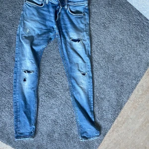  Jeans från Nudie - Säljer ett par ljusblå jeans från Nudie med slitna detaljer och hål på benen för en riktigt edgy look. Klassiska femficksmodellen, snygga kontrastsömmar och Nudie-logga på bakfickan. Perfekta om du gillar streetstyle och vill sticka ut.