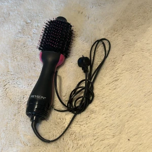 Revlon svart och rosa varmluftsborste - Säljer en elektrisk varmluftsborste från Revlon i svart och rosa. Borsten har täta borststrån med rosa toppar och ett ergonomiskt handtag. Perfekt för att styla och ge volym till håret med en smidig 2-i-1 funktion.