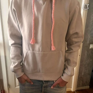 Ljusgrå hoodie från Sina world  - Säljer en ljusgrå hoodie från SNAK med feta rosa snören och stort rosa tryck på huvan.  Storlek M helt ny taggs finns
