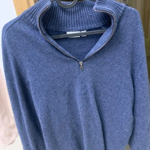 Blå stickad tröja med half zip från JJ - Mysig blå stickad tröja med ribbad hög krage och half zip-dragkedja. Perfekt för kyliga dagar och enkel att styla med jeans. Tröjan har lång ärm och en klassisk, avslappnad passform. Hör av er vid frågor!!!