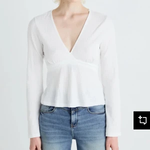 Vit omlottopp med knyt i ryggen - Vit omlottopp med v-ringning och långa ärmar. Toppen har en lätt strukturerad yta och knytband i ryggen som ger en extra detalj. Använd en gång till ett specifikt tillfälle utan några defekter. 