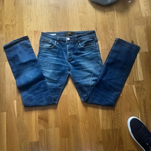 Jack & Jones Clark Regular Fit Jeans - Snygga blå jeans från Jack & Jones, modell Clark Regular Fit. Klassisk femficksdesign med raka ben och normal passform. Jeansen har en cool tvättad look och är tillverkade i slitstarkt bomullsjeansmaterial. Perfekta för dig som gillar en tidlös och avslappnad stil.