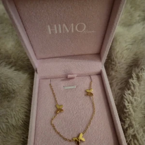 Guldigt halsband med fjärilar från HIMO - Supersött halsband från HIMO med små fjärilar i guld på en tunn kedja. Kommer i en lyxig rosa ask som gör det extra fint att ge bort. Perfekt för dig som gillar detaljer och vill ha något som sticker ut lite extra. OBS asken ingår inte.