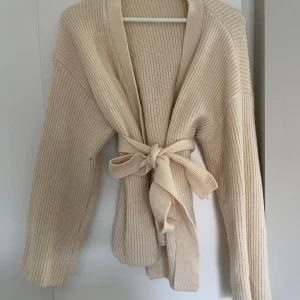 Beige ribbad kofta med knytband - Mysig beige kofta i ribbstickat material med långa ärmar och ett brett knytband i midjan🧡💛