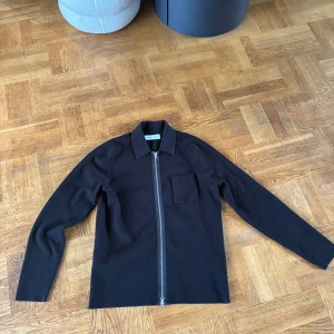 Svart kofta med dragkedja från Samsøe - Stilren svart tröja från Samsøe Samsøe med hel dragkedja framtill och en krage. Tröjan har en bröstficka och är långärmad.