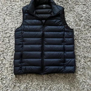 Svart dunväst från Uniqlo  - Säljer en svart dunväst från Uniqlo Ultra Light Down i storlek XS. Västen har horisontella quiltade paneler, hög krage och dragkedja framtill. Materialet är lätt och smidigt, perfekt för lager-på-lager. Enkel och stilren design som funkar till många outfits.