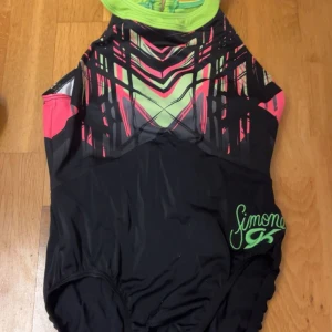 Gymnastikdräkt - Snygg gumnastikdräkt från Vera sport med grafiskt mönster i neonfärger som limegrönt och rosa upptill, svart nedtill och coolt tryck på bröstet. Hög halsringning och sportig passform.