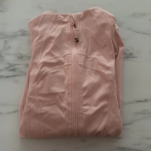 Ljusrosa träningsjacka från Lululemon - Supersnygg ljusrosa träningsjacka från Lululemon som tyvärr inte kommer till användning här, den är använd ett fåtal gånger.💞 