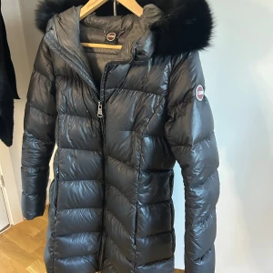 Svart dunjacka med päls från Colmar - Snygg svart lång dunjacka från Colmar med glansig finish och stor huva med bred päls. Jackan har dragkedja framtill, två fickor med dragkedja och quiltad design. Perfekt för kalla dagar när du vill vara både varm och stilren. Jackan är köpt från miinto är i storlek 42 (colmar storlekar) vilket motsvarar s/m. Passar mig perfekt som är S vanligtvis. 