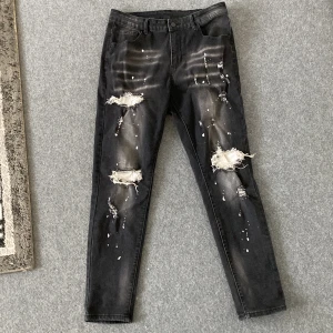 Svarta skinny jeans med slitningar från SHEIN - Svarta jeans från SHEIN i skinny fit med coola slitningar och hål på knäna. Byxorna har vita färgstänk och en tvättad look som ger en edgy vibe. Klassisk femficksmodell och knappstängning. Materialet är bomull med lite elastan för skön stretch.