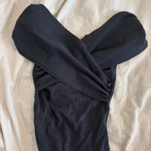 Svart omlott body från Zara - Svart omlott body från Zara i mjukt material med offshoulder-design. Bodyn har snygga draperingar och knytdetalj i midjan som ger en cool siluett. Perfekt för dig som gillar stilrena och trendiga plagg med en twist.