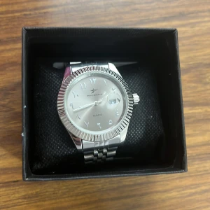 Silverfärgad klocka med arabiska siffror - Stilren klocka i silverfärg med rund boett och arabiska siffror på urtavlan. Finns extra delar i lådan för förlängning!!! Priset kan diskuteras.