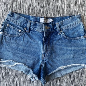 Blå jeansshorts från & Other Stories - Snygga blå jeansshorts från & Other Stories med råa, fransiga kanter och klassisk femficksdesign. Modellen är högmidjad och har en knapp och dragkedja framtill. Perfekta för varma dagar och har en cool, avslappnad vibe. Mått Midjan: ca 39 cm  100% bomull  Kommer från ett djur och rökfritt hem.