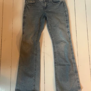 Ljusblå bootcut jeans med låg midja - Säljer ett par grå jeans med bootcut-modell och låg midja. Jeansen har klassisk femficksdesign, snygga bakfickor med lock och knapp samt en tvättad look. Perfekta för dig som gillar en avslappnad men trendig stil. Storlek 164/xs/32 men passar också s.💕💕