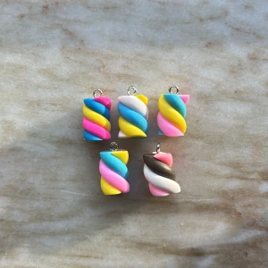 Färgglada marshmallows berlocker - Fem stycken marshmallows berlocker i glada färger som rosa, blå, gul, vit och brun. Perfekta att använda som hängsmycke till halsband eller armband. De har ett lekfullt, randigt mönster och är tillverkade i syntetmaterial med metallögla för enkel montering.