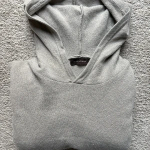 Kashmir Hoodie från Oscar Jacobsson. - Kashmir Hoodie från Oscar Jacobsson. Grå/Beige färg med väldigt mjukt material. Storlek S. Passar mellan längderna 175-185 cm beroende på hur man vill att den ska sitta. Passar till allt och kan användas i alla tillfällen.