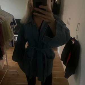 Jjeansjacka från NA-KD - Säljer en oversized jeansjacka från NA-KD i klassisk blå denim. Jackan har breda ärmar, stora fickor och knytskärp i midjan för en avslappnad look. .