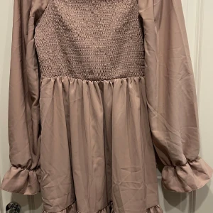 Beige långärmad klänning från SHEIN - Supersöt beige klänning från SHEIN med smockad överdel och långa puffärmar med volang vid ärmslutet. Kjolen är lätt rynkad och ger en flowy känsla. Perfekt för dig som gillar en feminin och trendig look.