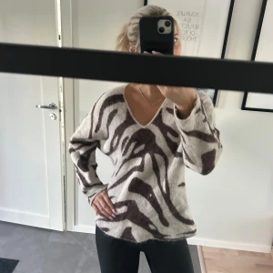 Beige zebramönstrad stickad tröja - Stickad tröja från Wera i beige med mörkbrunt zebramönster. Tröjan har v-ringning, lång ärm och en loose passform. Storlek S och bra skick.