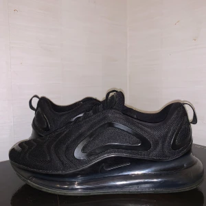 Nike Air Max 720 svarta sneakers - Svarta Nike Air Max 720 sneakers med futuristisk design och vågiga detaljer på ovandelen. Skorna har en tjock, genomskinlig plattformssula och är tillverkade i mesh och syntetmaterial. Snygga snörningar och diskret Nike-logga på sidan. Perfekta för dig som gillar streetstyle.