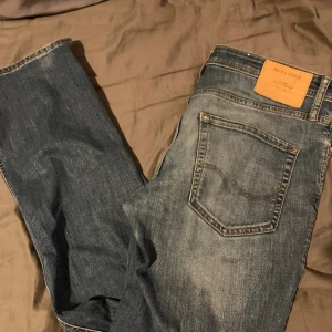 Jack & Jones Slim Fit jeans blå - Snygga blå jeans från Jack & Jones i modellen Slim Fit Tim. Jeansen har klassisk femficksdesign, ljus tvätt med slitningar och kontrastsömmar. Passformen är slim och materialet är robust denim. Perfekta för dig som gillar en smal siluett och stilren look.