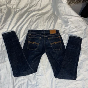 Nudie jeans - Snygga mörkblå jeans från Nudie Jeans med klassiska orange sömmar och ikoniska bakfickor. Modellen har en smal passform och raka ben. Tillverkade i slitstarkt bomullstyg, perfekta för dig som gillar stilrena och tidlösa jeans.