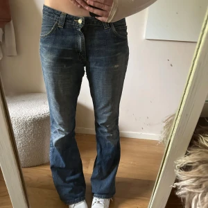 Blå bootcut jeans från Lee - Säljer ett par klassiska blå jeans från Lee med bootcut passform och låg midja. Jag är 175! Jeansen har snyggt slitna detaljer, fem fickor och Lee-logga bak i midjan. Perfekta för dig som gillar en avslappnad och tidlös look.